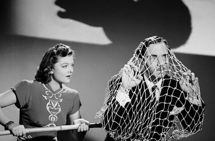 A screwball comedy still: a woman beside a man caught in a fishing net