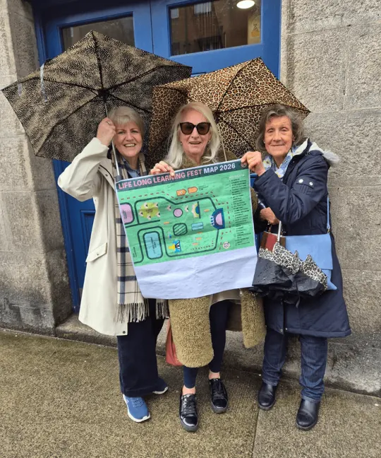 Three women under umbrellas holding up the Lifelong Learning Festival map