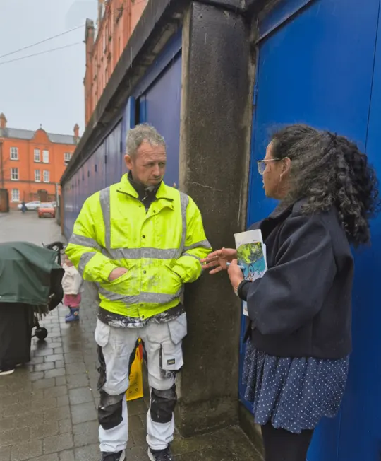 A worker in a hi-vis jacket reading a festival leaflet handed to him on the street