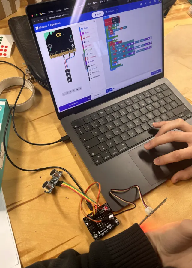 Laptop running the micro:bit editor beside a wired sonar sensor on a workbench