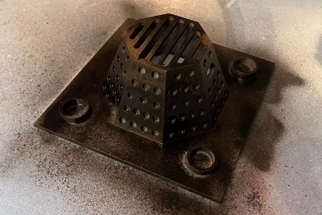 Perforated metal furnace insert, scorched, sitting on its base plate
