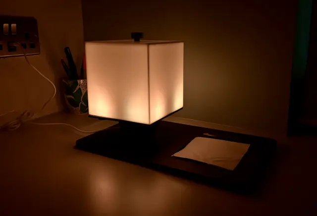 NOX resting on its tray in a dark room, glowing a soft warm white