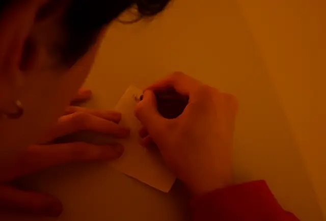 Hands writing a single line on a small slip of paper in warm light
