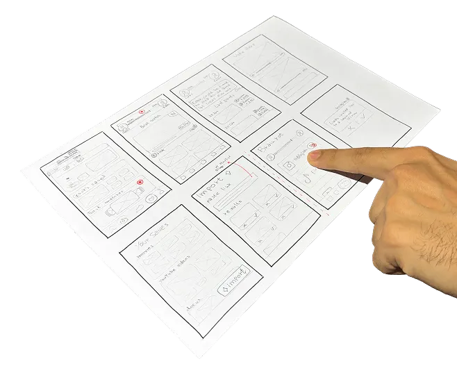 A finger pointing at a hand-drawn paper wireframe