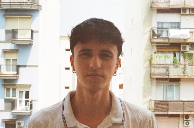Colour portrait of Ludovico Galassi in a white polo shirt, standing on a balcony between apartment blocks