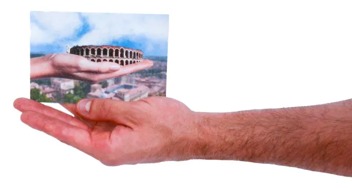 A hand holding a postcard of the Arena