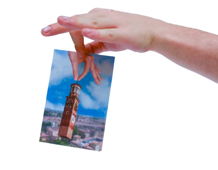 A hand holding a postcard of the Torre dei Lamberti