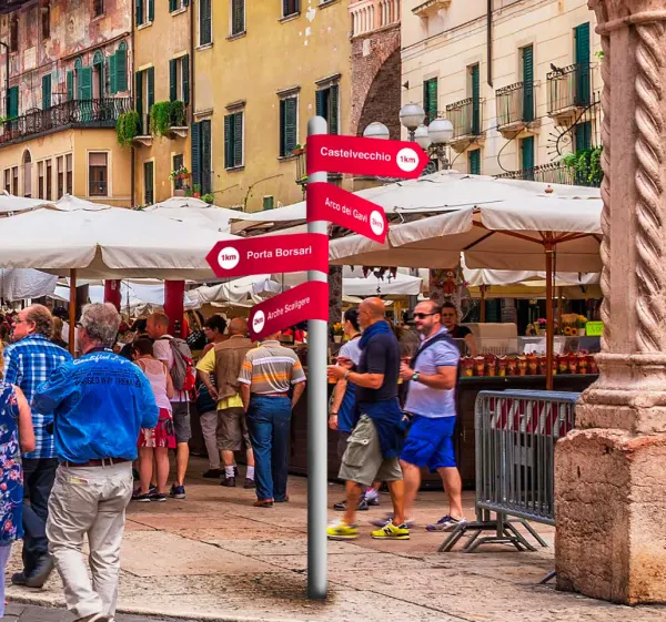 Crimson directional signs in a crowded Verona square