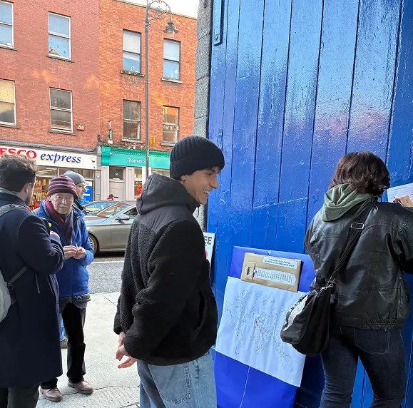 Passers-by stopping at the probe on a street corner, a Tesco Express behind them